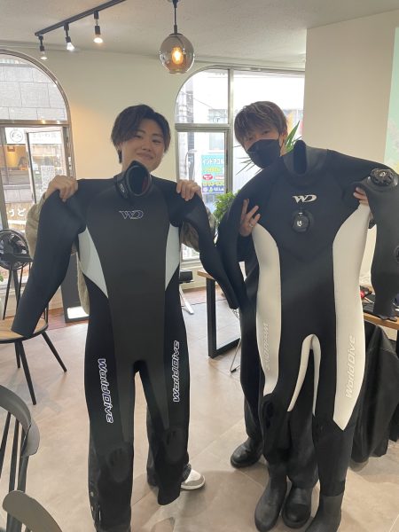 男性ダイバー二人が新しいスーツを手に取って写真を撮っている様子